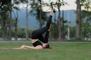 Asian woman practicing yoga peacefully in the park after work, finding relaxation and balance at...