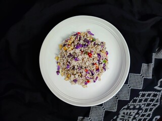 a plate of fried rice with vegetables and chili sprinkled on a table covered with black cloth