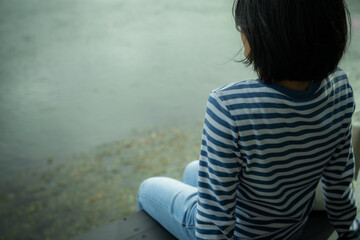 Woman sitting by water on rainy day. Contemplation and nature reflection in tranquil moment of...