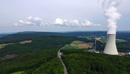 High-angle view of a power plant amidst a lush green landscape, with billowing white smoke rising from the cooling towers.