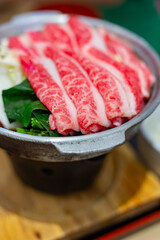 Japanese tasty sukiyaki dish for one person, featuring delicious wagyu beef, fresh vegetables and a raw egg in the restaurant.