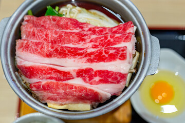 Japanese tasty sukiyaki dish for one person, featuring delicious wagyu beef, fresh vegetables and a raw egg in the restaurant.