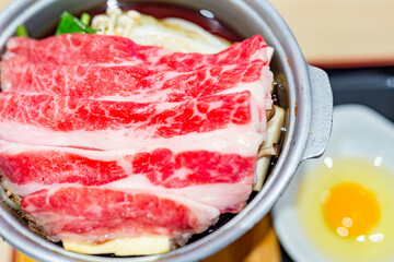 Japanese tasty sukiyaki dish for one person, featuring delicious wagyu beef, fresh vegetables and a raw egg in the restaurant.