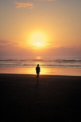 Fototapeta premium Solitary Figure Contemplating Ocean Sunset, Reflective Beach Scene, Peaceful Coastal Moment
