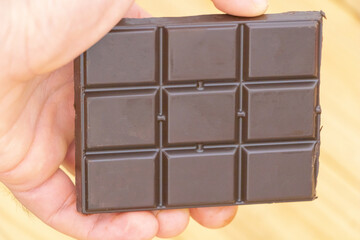 Hand holding dark chocolate bar with square pieces closeup