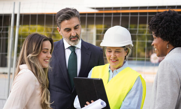 Architect showing building plans on a tablet to a group of investors and a businesswoman at a construction site