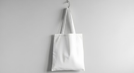 Blank white canvas tote bag hanging on a light grey wall, perfect for mockup designs, sustainable shopping, or promotional branding as a versatile blank canvas
