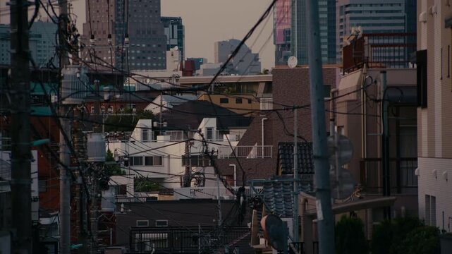 Peaceful Tokyo Evening Street Facing Shibuya with Silhouetted Power Network &ndash; Apartment building and power lines stand dark against glowing horizon with sunset colors above.