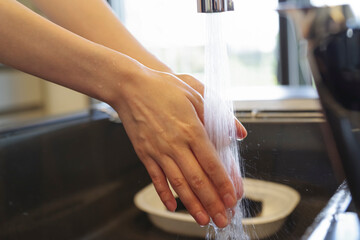 キッチンで手を洗う女性の手元（顔なし）