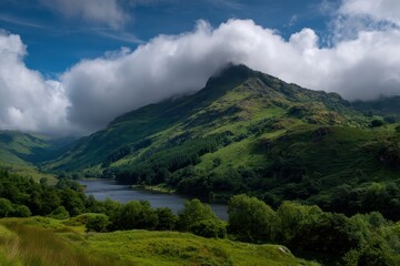 Obraz premium A lush, green mountain landscape with a river and dramatic clouds hanging over the peak under a bright blue sky
