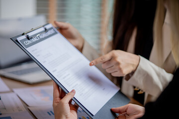 Businesswomen in office examining financial documents, discussing strategy, planning, and agreements with paperwork, contracts, communication, analysis, and cooperation.