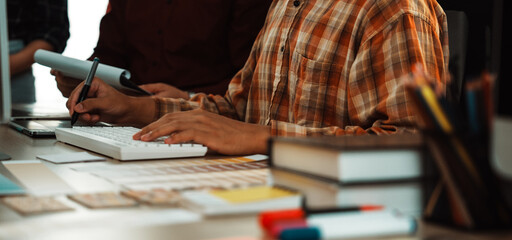 A professional designer is engaged in a digital project at a modern desk, surrounded by papers, colorful markers, and a collaborative team, fostering creativity and innovation. SACTR