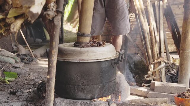 alcohol production in Flores, Indonesia, with bamboo pipe attached to metal pot over firewood flames, distilling palm sap into traditional village liquor known as arak or sopi