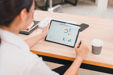 Businesswoman analyzing sales performance chart on digital tablet, reviewing data and graphs at...