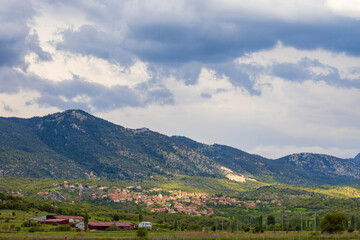 Landscape with red tiled roofs of houses small town among green forest on mountain slope under...