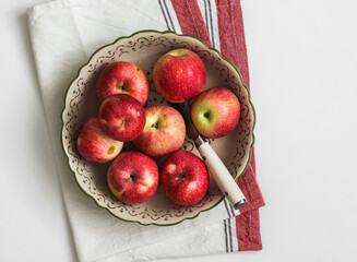 Fresh garden red apples in a bowl on a napkin on a white table, top view