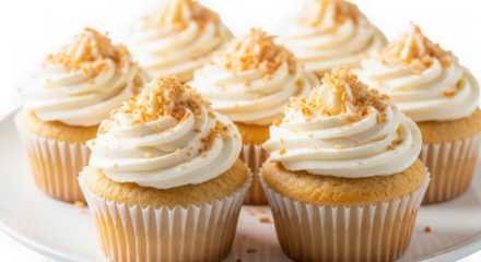 Six vanilla cupcakes with creamy white frosting and golden crunchy topping, arranged on a white plate, isolated on transparent background