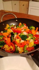 A wok of colorful roasted vegetables, including broccoli, bell peppers, and potatoes, sits on a stovetop