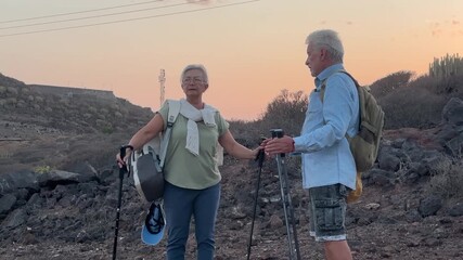 Happy senior couple in their seventies hiking together in a desert landscape during active vacation weekend, outdoor physical activity, trekking, healthy lifestyle, walking adventure and nature explor - Powered by Adobe