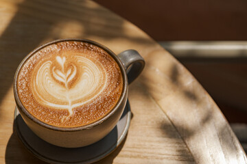 latte coffee art on wooden plate at desk in sun shine with shade of the tree