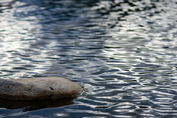 small rock on the still river steam with reflection of blue sky and shade wave from wind blow