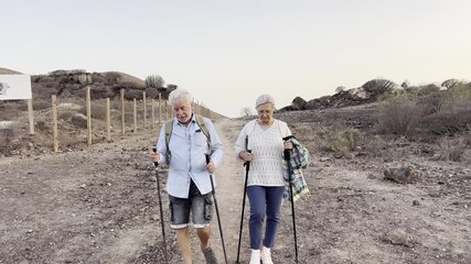 Happy senior couple in their seventies hiking together in a desert landscape during active vacation weekend, outdoor physical activity, trekking, healthy lifestyle, walking adventure and nature explor