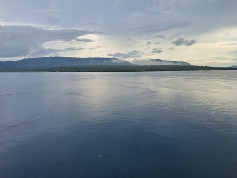 Vast calm lake reflecting distant mountains under a cloudy sky.