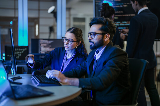 A diverse team of AI developers shares a successful moment in the office. A female programmer smiles as they review the positive results of a complex machine learning algorithm.