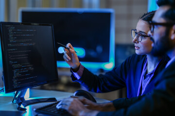 diverse AI developers collaborate in a late-night coding session. A senior engineer mentors his colleague as they program a complex machine learning algorithm together.