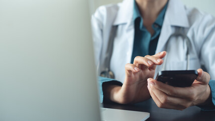 Female doctor using smartphone at doctor's office, messaging with patient, prescribing treatment with laptop computer on table at medical clinic, closeup, health care and medicine, consultation online