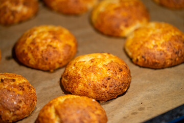 Freshly baked cheese buns cooling on parchment paper. The buns have a golden-brown crust, indicating perfect baking. Ideal for illustrating homemade baking or culinary delights.
