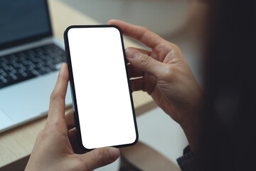 Using smartphone, white screen mockup. Woman using mobile phone with blank white screen during working with laptop on table, mockup for social media marketing ads