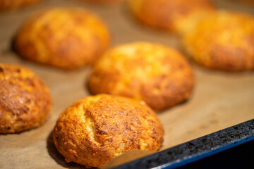Freshly baked cheese buns cooling on parchment paper. The buns have a golden-brown crust, indicating perfect baking. Ideal for illustrating homemade baking or culinary delights.
