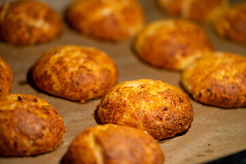 Freshly baked cheese buns cooling on parchment paper. The buns have a golden-brown crust, indicating perfect baking. Ideal for illustrating homemade baking or culinary delights.
