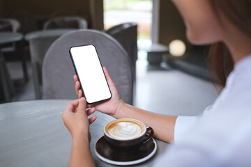 Mockup image of a woman holding and using mobile phone with blank desktop screen in cafe
