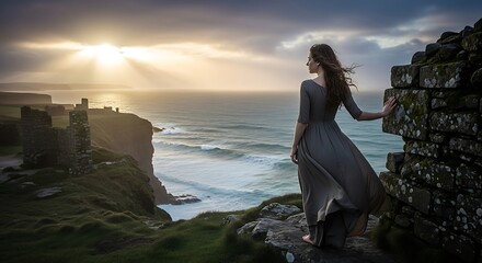 Woman in flowing gown at castle ruins overlooking the sea at sunset.