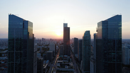 Fototapeta premium Aerial view of a modern city skyline with skyscrapers at sunset casting a warm golden glow on the buildings