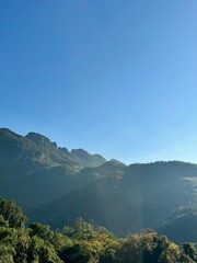 Majestic mountain ranges covered in lush green forests under a clear, beautiful blue sky on a sunny day.