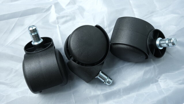 Set of black swivel caster wheels with metal stems, typically used for office chairs, placed on a white crinkled background.
