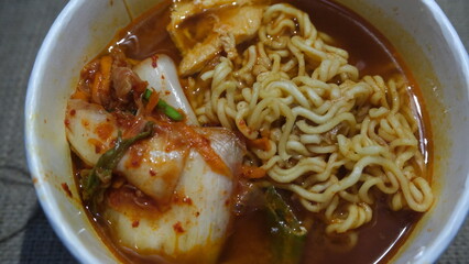 Bowl of Korean ramen noodles in rich red broth, served with kimchi, tofu, and vegetables for a flavorful, spicy comfort meal.