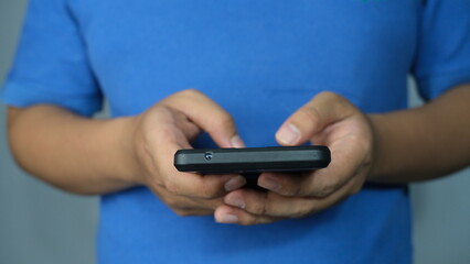 Close-up of a person in a blue shirt holding a smartphone with both hands, focused on screen interaction and digital communication.