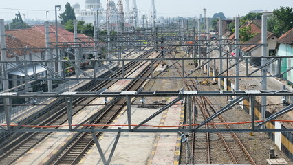 Multiple railway tracks run through a quiet city train station under overhead power lines, showing a clean and structured transport hub.
