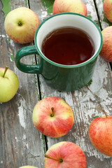 Green enamel mug with hot tea and fresh apples on old wooden table