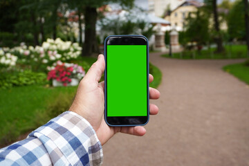 Man holding smartphone with green screen in park