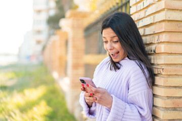 Young woman at outdoors surprised and sending a message