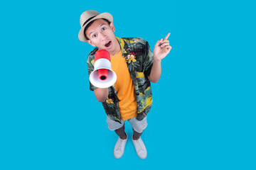 Tourist Man Holding A Megaphone And Pointing Up, Looking Surprised Against a Blue Background