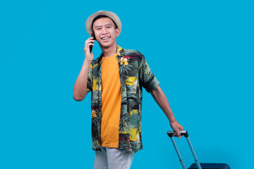 A Happy Young Asian Man In A Hawaiian Outfit, Talking On A Smartphone While holding A Suitcase...
