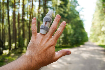 Man showing injured finger with splint in forest road