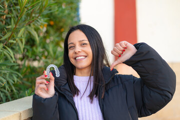Young woman holding invisible braces at outdoors proud and self-satisfied