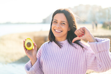 Young woman at outdoors holding an avocado at outdoors proud and self-satisfied